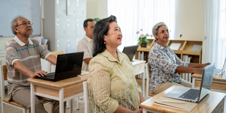 Elderly Adults Attending Educational Session With Laptops in Classroom Setting Memory Care Facility