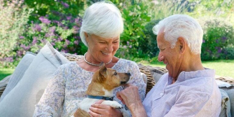 Elderly Couple Holding Therapy Dog Outdoors at Memory Care Facility